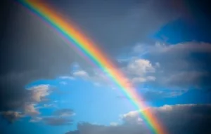 Photo of a rainbow against a blue sky with clouds 